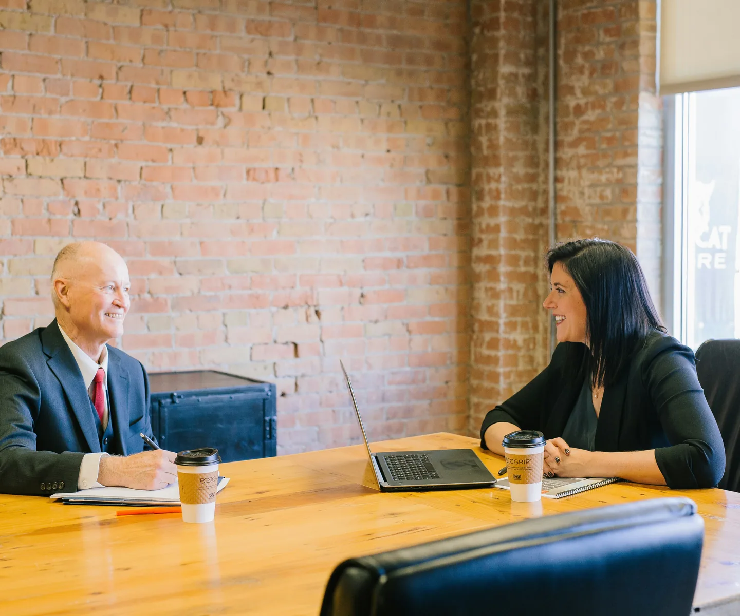 Two business professionals in conversation across a worktable in a bright office